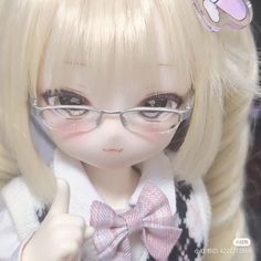 a doll wearing glasses and a bow tie giving the thumbs up sign with her hand