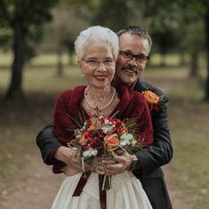 an older couple embracing each other in the park with flowers on their wedding day,