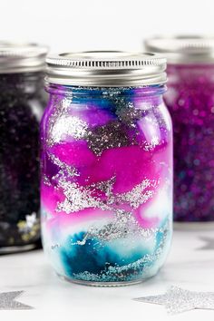 three jars filled with different colored glitters on top of a white table next to stars