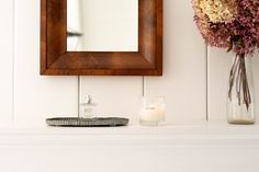 a wooden mirror sitting on top of a mantle next to a vase filled with flowers