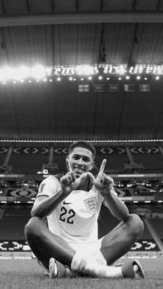 a man sitting on the ground in front of a soccer stadium holding his fingers up