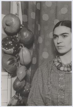 an old black and white photo of a woman standing next to some fruit hanging on the wall