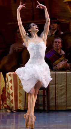 the ballerina is wearing a white dress and has her arms outstretched in the air