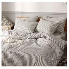 a bed with striped sheets and pillows on top of it, next to a white wall