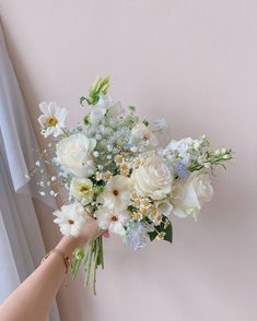 a woman holding a bouquet of white and blue flowers in her hand next to a window