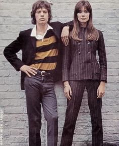 two people standing next to each other in front of a brick wall