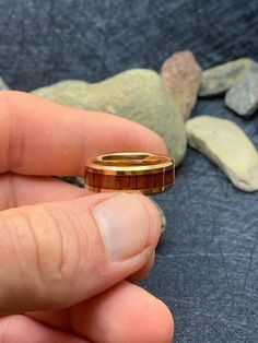 a hand holding a gold ring in front of some rocks and stones on the ground