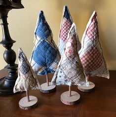 three small christmas trees made out of fabric on top of a wooden table next to a lamp