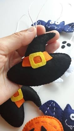 a hand is holding an orange and black witch's hat ornament next to other halloween decorations