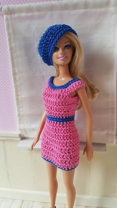 a barbie doll wearing a pink dress and blue hat is standing in front of a white curtain