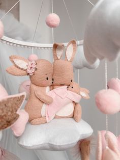 two stuffed bunnies are hanging from a mobile in the shape of rabbits on a cloud with pink pom poms