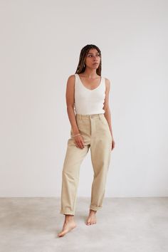 a woman standing in front of a white wall wearing khaki pants and a tank top