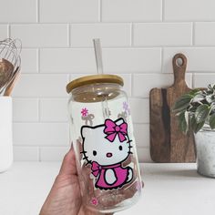 a hand holding a hello kitty tumbler next to a kitchen counter with utensils