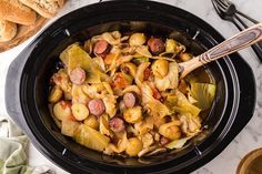 a crock pot filled with pasta and sausage next to bread on a marble table