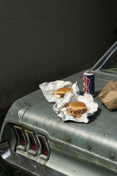 two sandwiches are sitting on the hood of an old car next to a can of soda