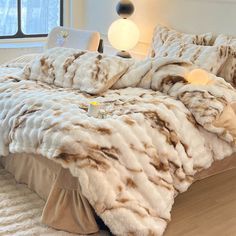 a bed covered in white and brown fur next to a window with a lamp on top of it