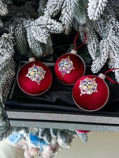 two red ornaments are sitting on a black box next to some pine cones and christmas tree branches