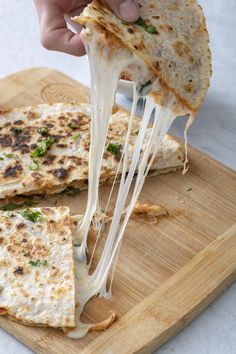 a person is taking a slice of quesadilla from a cutting board