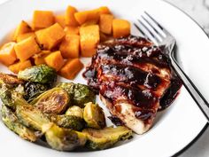 a white plate topped with chicken, brussel sprouts and sweet potatoes