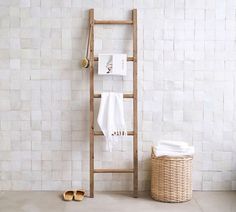 a white bathroom with a ladder leaning against the wall next to a basket and towel rack