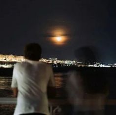 two people looking out over the water at night with a full moon in the background