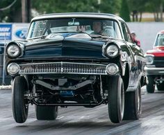 an old car driving down the street with other cars in the background