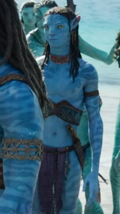 some people are standing in the water with blue paint on their body and one person has dreadlocks