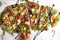 a person holding a slice of pizza on top of a white table with green and red toppings