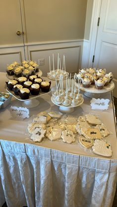 a table topped with cupcakes and desserts on top of white cloth covered tables