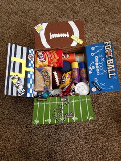 an open football box filled with candy and sports related items on top of a carpeted floor