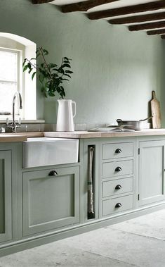 a kitchen with green painted cabinets and white counter tops, an open window above the sink