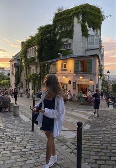 a woman walking down the street in front of a building with vines growing on it