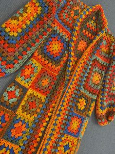 a multicolored crocheted jacket laying on top of a gray surface