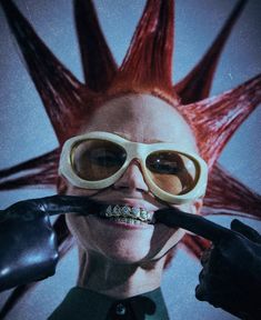 a woman with red hair and goggles holding a toothbrush in front of her mouth