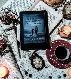 a book sitting on top of an open book next to a cup of coffee and candles