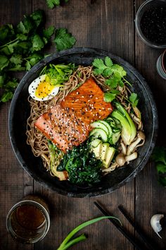 a bowl filled with noodles and vegetables next to chopsticks on a wooden table