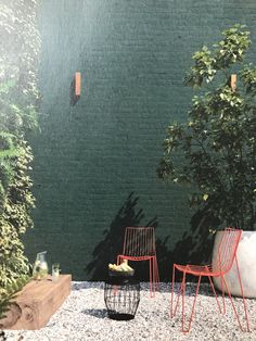 two chairs sitting next to each other in front of a green brick wall and trees