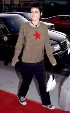 a woman is walking down the red carpet with her hand in her pocket and holding a white bag