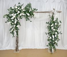 two white flowers and greenery in front of a white backdrop for a wedding ceremony