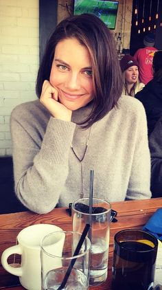 a woman is sitting at a table with her hand on her chin and looking into the camera