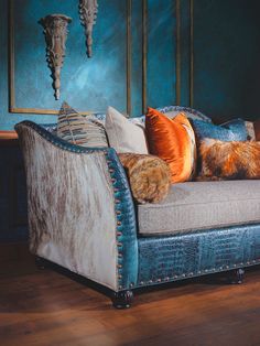 a couch with several pillows on it in front of a blue wall and wooden floor