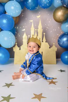 a baby sitting in front of blue and gold balloons