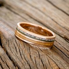 two gold wedding bands sitting on top of a piece of wood with one ring in the middle