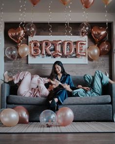 two women sitting on a couch with balloons and streamers in front of the wall