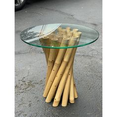 a table made out of bamboo sticks and glass top sitting on the ground next to a parked car