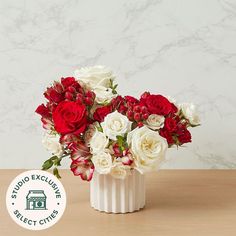 a white vase with red and white flowers in it on a table next to a sign that says studio exclusively select cities