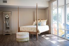 a bedroom with a four poster bed and wooden flooring next to a large window