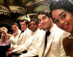 a group of people sitting next to each other in front of a crowd wearing white suits and black ties