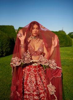 a woman wearing a red wedding dress and veil with her hands up in the air