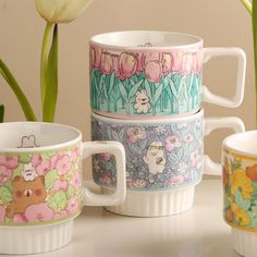 four coffee mugs with flowers painted on them and one has a bear in the middle